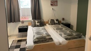 A bedroom with two beds, a window with curtains, a wall-mounted lamp, and a small table with a lamp. - Appartement Wasserfall by Interhome (Stall)