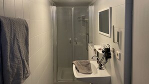 A small, enclosed shower area with a glass door, a white sink with a towel, and a mirror above the sink. - Appartement Wasserfall by Interhome (Stall)