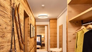 Ein Holzinnenraum mit einer Diele, die zu einem Schlafzimmer führt, mit Ski-Ausrüstung an der Wand und einem Kleiderständer.