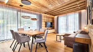 Ein modernes Wohnzimmer mit Holzboden, einer Essecke mit Holztisch und -stühlen sowie einer Sofagarnitur.