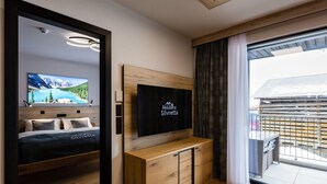 Una habitación de hotel moderna con una cama, un televisor montado en la pared, un armario de madera y un ventanal con cortinas.