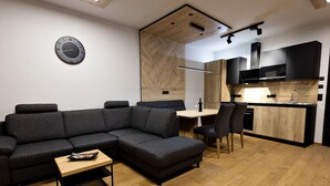 Un espacio habitable moderno con un sofá modular, una mesita de madera, un área de comedor con sillas y una cocina con armarios oscuros y encimera de madera.