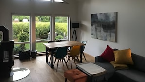 Uma sala ampla com uma mesa de jantar, cadeiras, um sofá e uma janela grande com vista para um jardim.