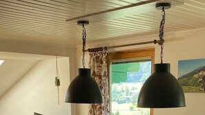 Ruokailutila, jossa on puinen pöytä ja tuolit, riippuvalaisin ja ikkunasta avautuva näkymä ulos.