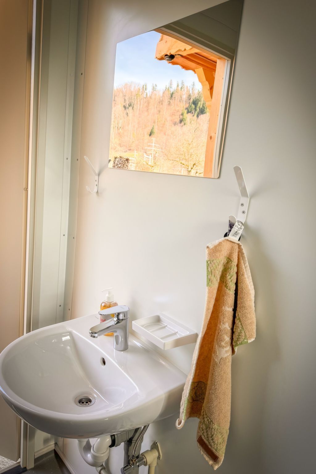 A bathroom with a white sink, a window with a view of trees, and a towel hanging on a rack.