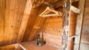 Een slaapkamer met een houten zolder, schuine plafond, een klein tafeltje en een hangende houten kapstok.