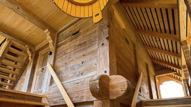 Een houten interieur met een wenteltrap en een rond dakraam.