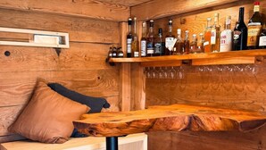 Een houten bar met flessen en glazen, een kussentje en een rieten mand.