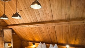 Een knus slaapkamer in een houten chalet, met een bed, twee nachtkastjes en hangende hanglampen.