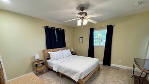 Ein Schlafzimmer mit einem Bett, Nachttischen, einem Tisch, einem Deckenventilator und einem Fenster mit Vorhängen.