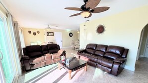 Ein Wohnzimmer mit zwei braunen Ledersofas, einem Glastisch, einem Deckenventilator und einer Wanddekoration im Sonnenstrahl-Design.