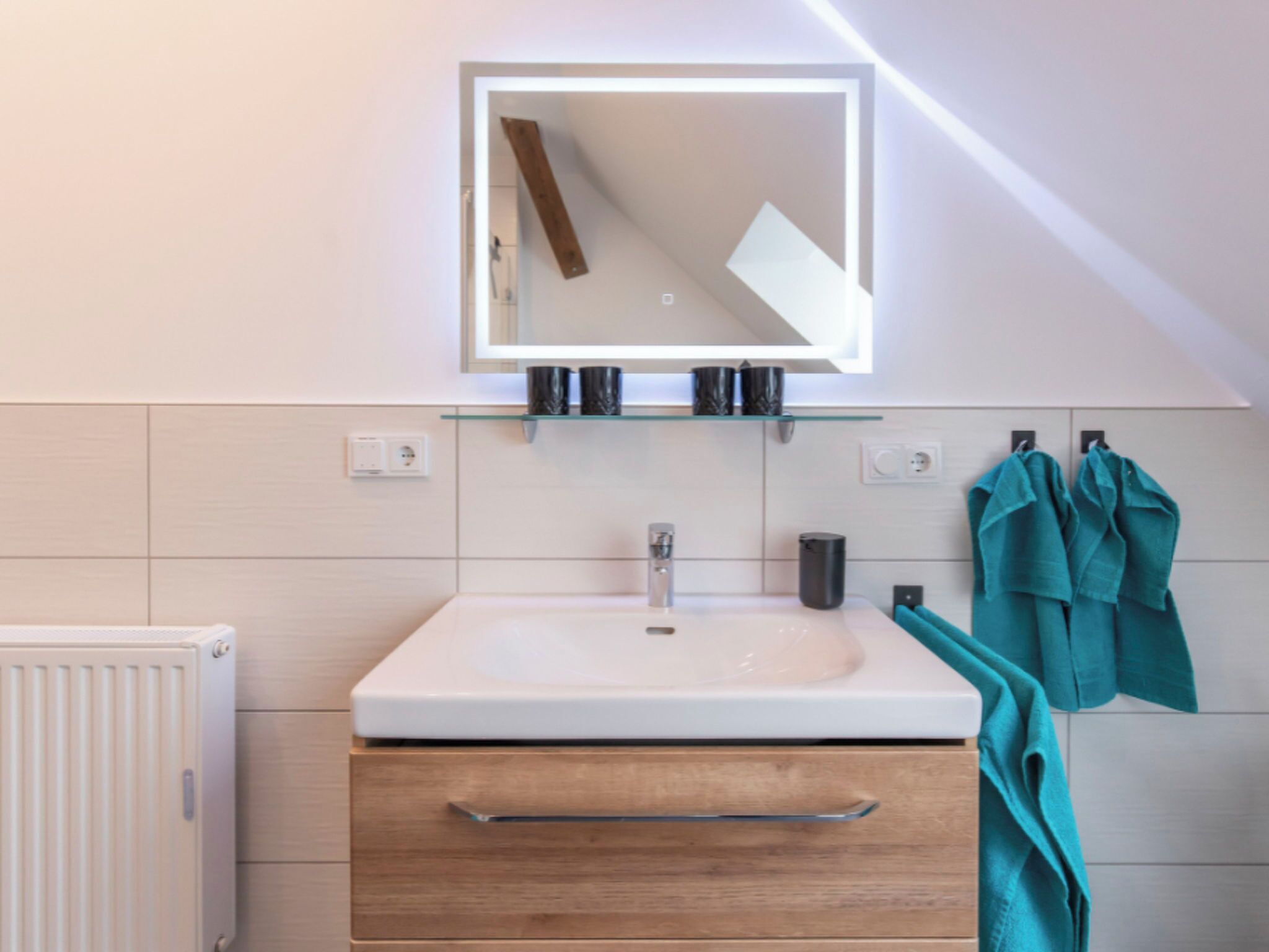 A modern bathroom with a white sink, a mirror, and a towel rack with teal towels.
