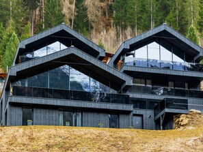 Un edificio moderno de varios pisos con fachada de madera y grandes ventanales, frente a un bosque.