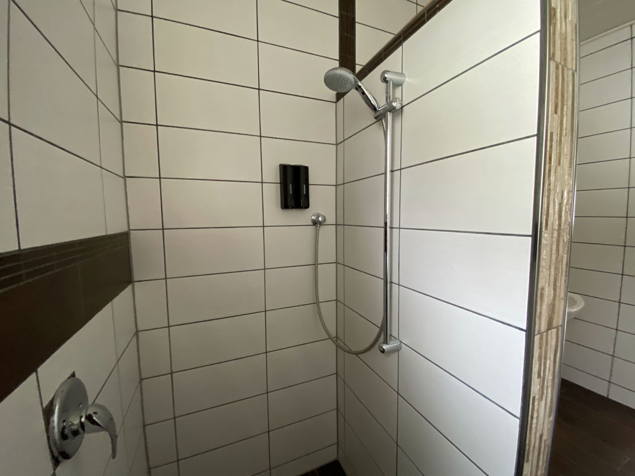 Um pequeno espaço de chuveiro revestido com azulejos, com chuveiro manual e torneira fixa na parede.