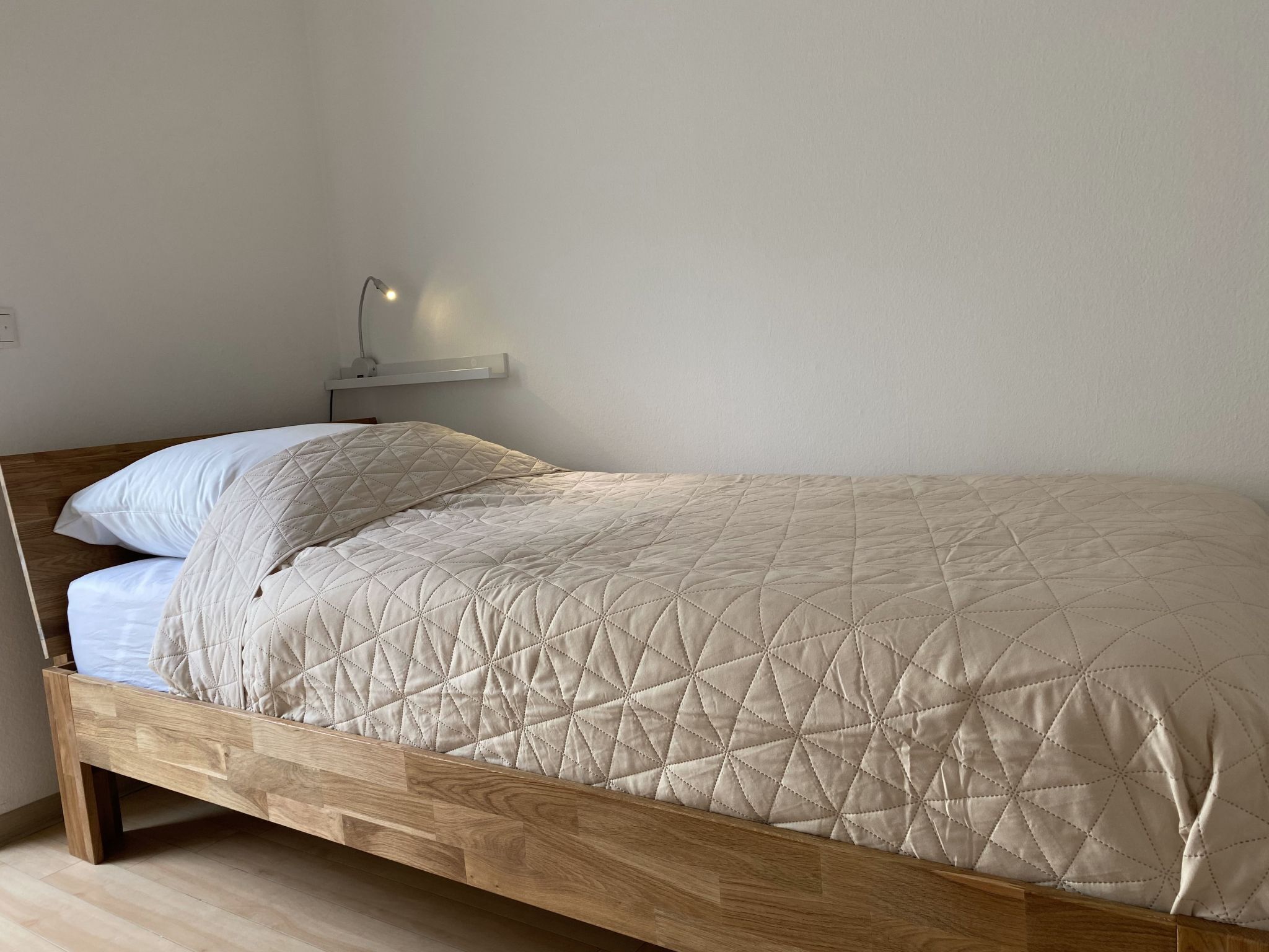 En enkel seng med træstel og et quiltet, beige dynebetræk.