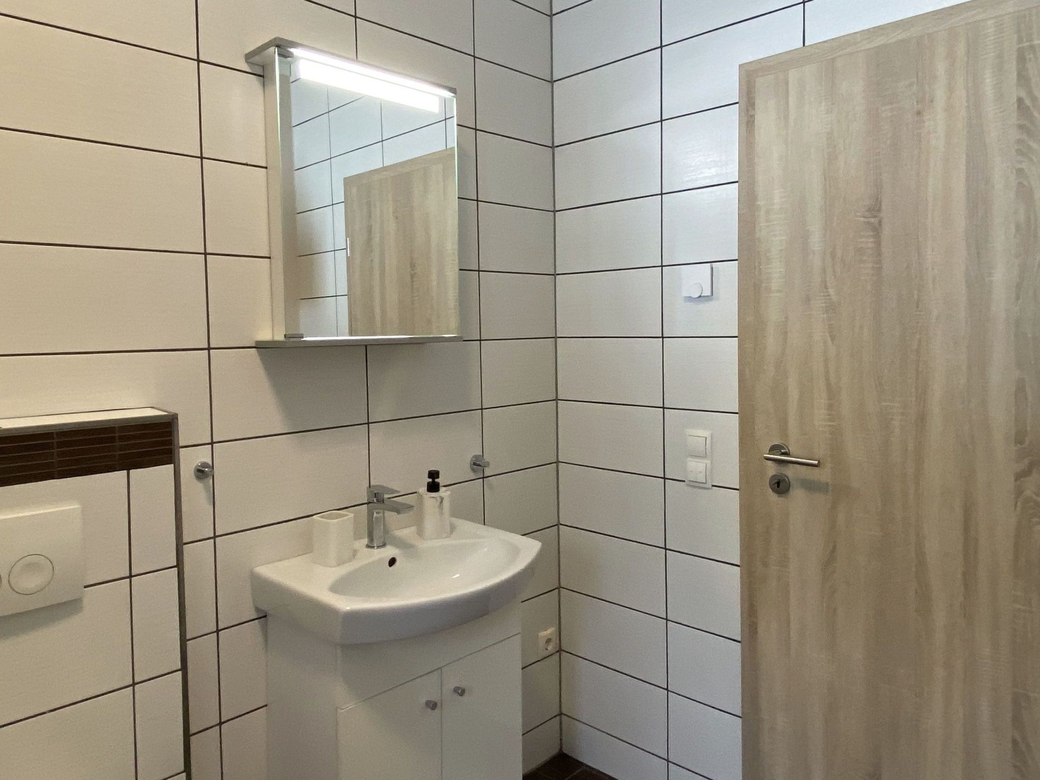A bathroom with white tiles, a sink, a mirror, and a door.