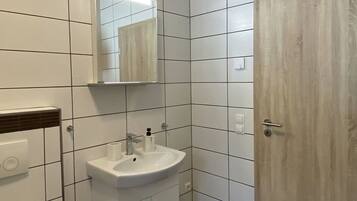 A bathroom with white tiles, a sink, a mirror, and a door.