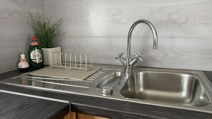 Una cuina amb un rentaplat de metall inoxidable, un escorredor, una ampolla de detergent Fairy i una planta en test.