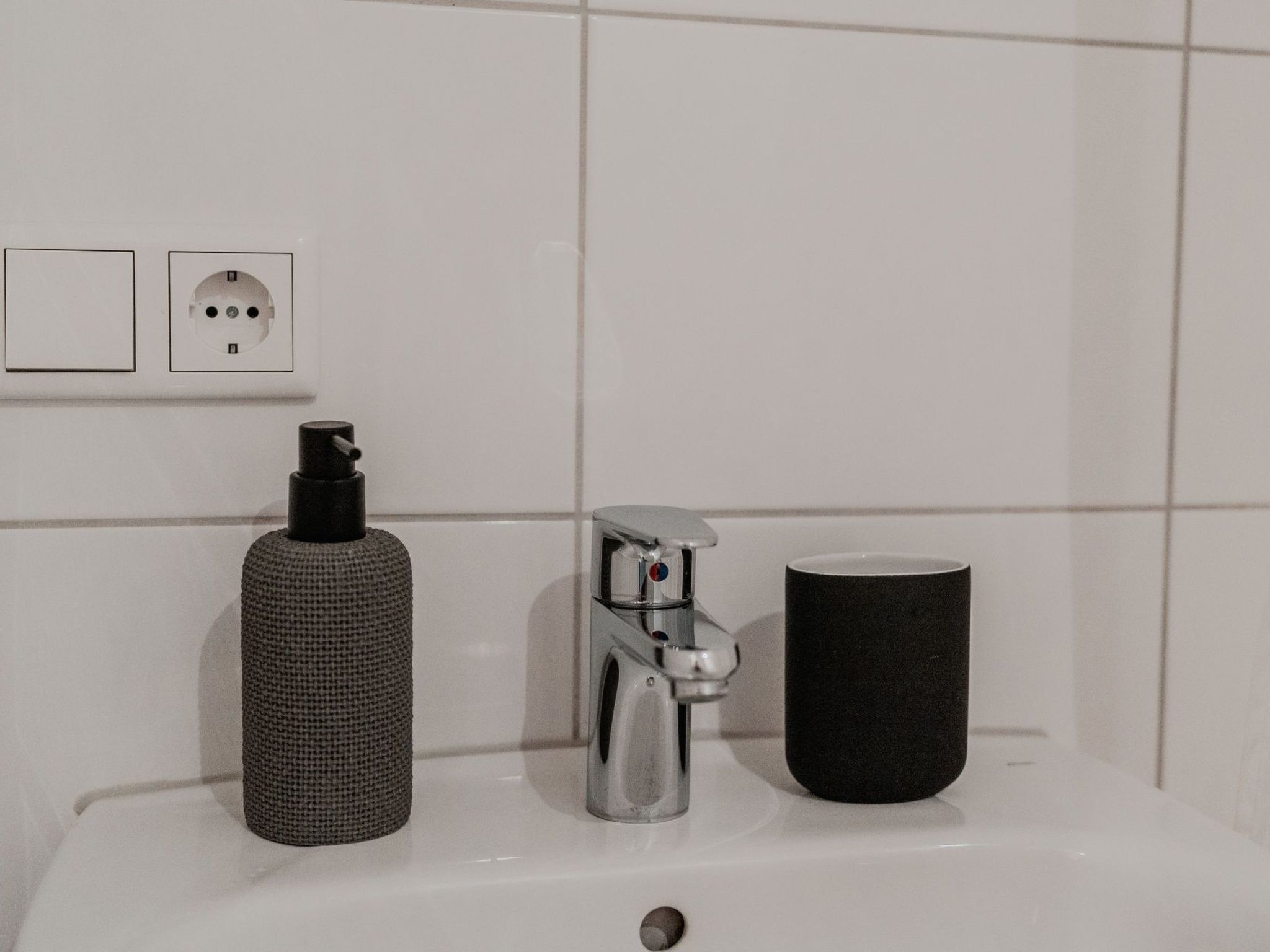 A bathroom sink with a soap dispenser, faucet, and a black mug.