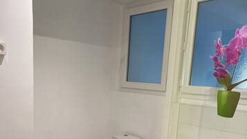A bathroom with a white toilet, a white sink, a black bath mat, and a window with a view of the outside.
