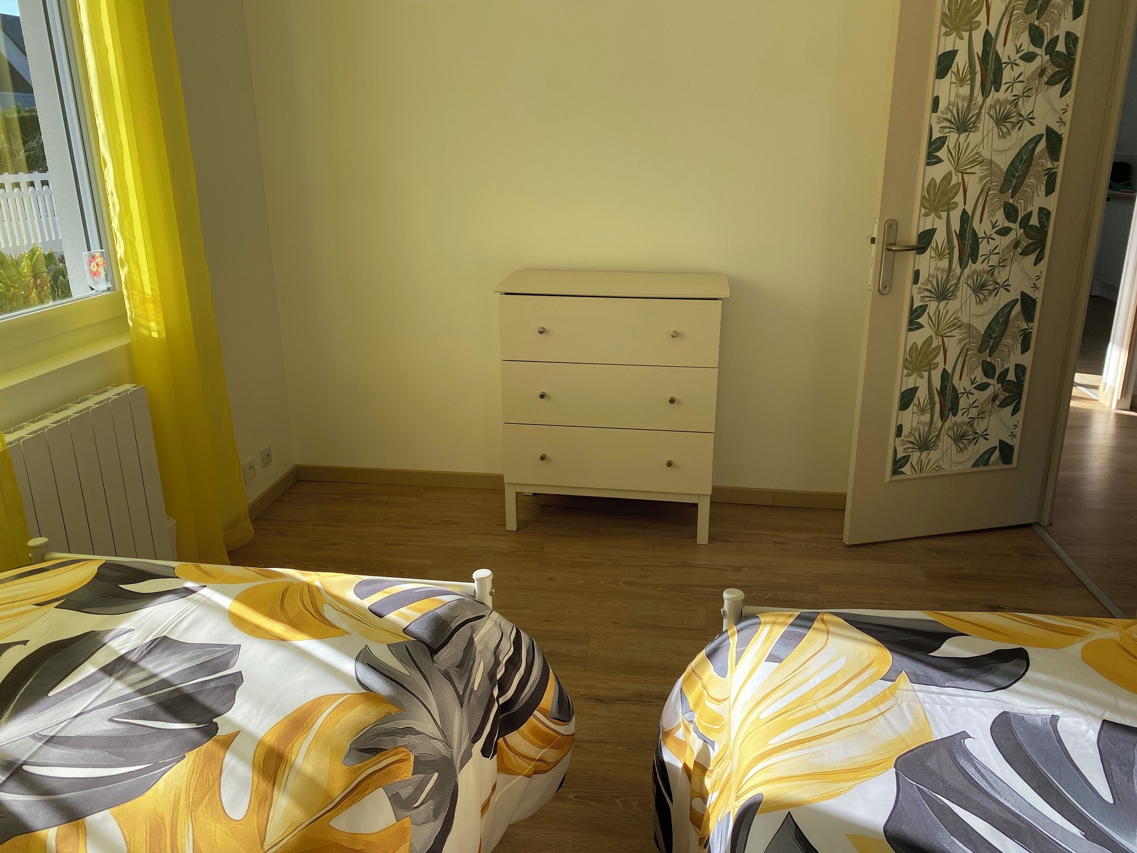 A bedroom with a bed, a white dresser, and a door with floral wallpaper.
