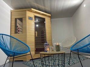 A sauna room with a wooden cabinet, two blue chairs, a small table with a candle, and a decorative item.