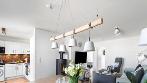 A modern kitchen with white cabinets, a built-in stove, and a dining area with a wooden table, chairs, and a vase of flowers. - Maltes-Ostseekoje by Interhome (Hasselberg)