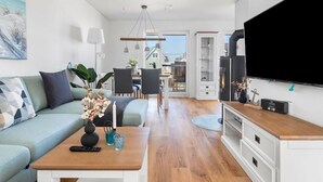 A modern living room with a sofa, coffee table, and TV. There is a dining area with chairs and a table. The room has wooden flooring and white walls. - Maltes-Ostseekoje by Interhome (Hasselberg)