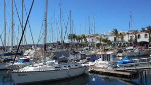 Marina con varios veleros amarrados, rodeada de edificios de arquitectura mediterránea.