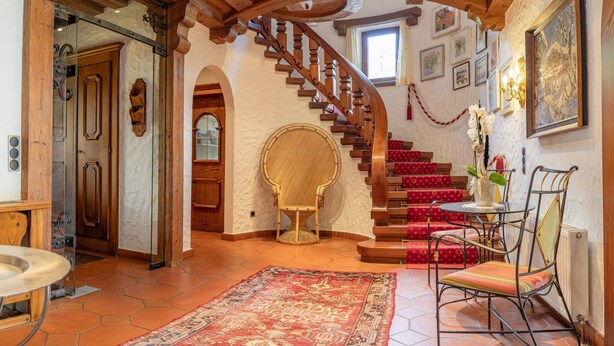 A spacious room with a wooden staircase, a round wicker chair, a dining table with chairs, and a red patterned rug. - Villa Emma, Ferienhaus für bis zu 10 Personen, eigener Garten, absolute Privats by Interhome (Kaltenbach)