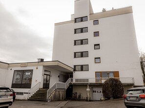 Ein mehrstöckiges Gebäude mit heller Fassade, einem gut erkennbaren Eingang und einer Treppe, die zum Erdgeschoss führt.