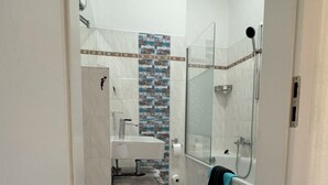 Et badeværelse med bruser, håndvask og toilet.