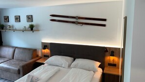 Ett modernt hotellrum med en säng, en soffa, ett träfärgat sänggavel, ett skiställ och vägghängda hyllor med dekorativa föremål.