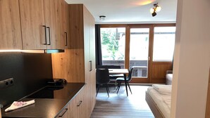 Ett modernt kök med träskåp och en svart bänkskiva, en matplats med bord och stolar samt ett sovrum med en säng.