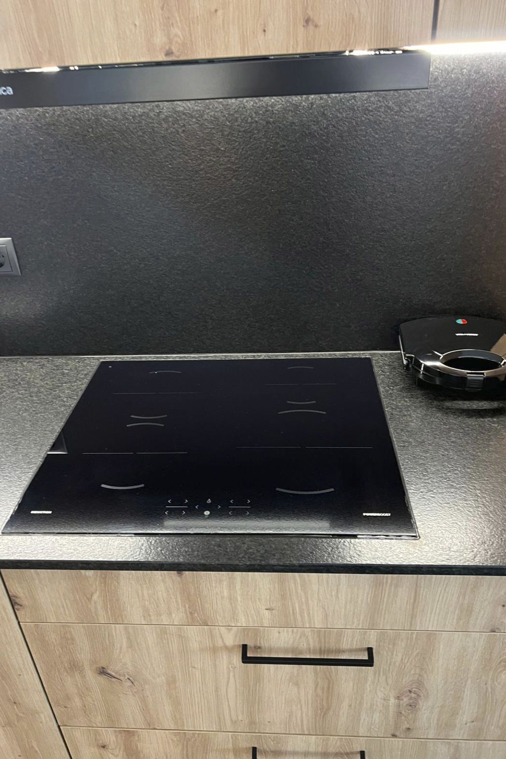 A kitchen with a black induction cooktop, a wooden cabinet below, and a black appliance on the countertop.