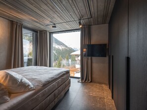 Un dormitorio moderno con una cama grande, un televisor de pantalla plana en la pared y vistas a montañas por la ventana.