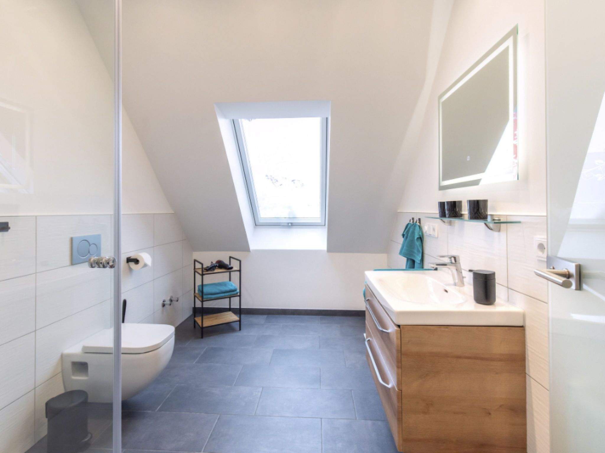 Une salle de bain moderne dotée d’un puits de lumière, de toilettes, d’un lavabo et d’un meuble-lavabo en bois.