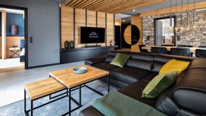 Una sala de estar moderna con techo de madera, un sofá de cuero negro, una mesa de centro de madera y un televisor de pantalla plana montado en una pared de madera.
