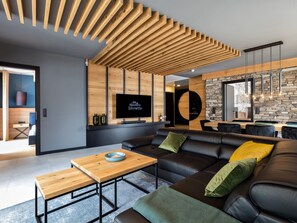 A modern living room with a wooden ceiling, a black leather sofa, a wooden coffee table, and a flat-screen TV mounted on a wooden wall. - Atemberaubendes Luxus-Apartment Residenz Silvretta by Interhome (See)