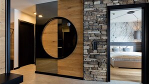 Un interior moderno con una pared de piedra, un panel de madera y un espejo circular.