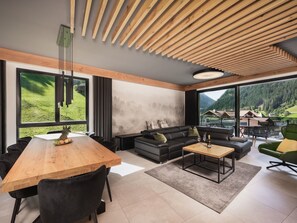 A modern living room with a wooden ceiling, large windows, a sofa, a coffee table, and a dining area with chairs and a wooden table. - Atemberaubendes Luxus-Apartment Residenz Silvretta by Interhome (See)