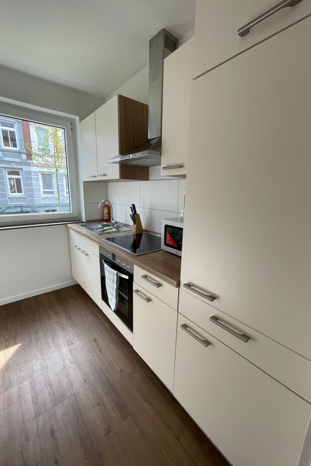 Ett modernt kök med vita skåp, en träbänkskiva och ett fönster som ger utsikt över omgivningen.
