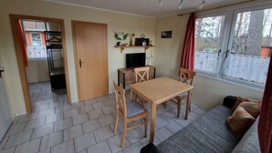 Ein kompakter Wohnbereich mit Essplatz, einer Couch, einem Fernseher und einem fensterbelaubten Fenster.