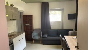Ein gemütlicher Wohnraum mit Küchenzeile, einer Couch, einem Esstisch und einem an der Wand montierten Fernseher.