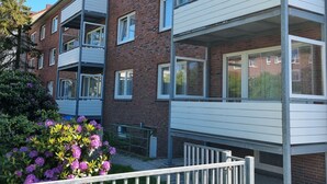 En fleretagers bygning med altaner, murstensfacade og en have med lilla blomster.