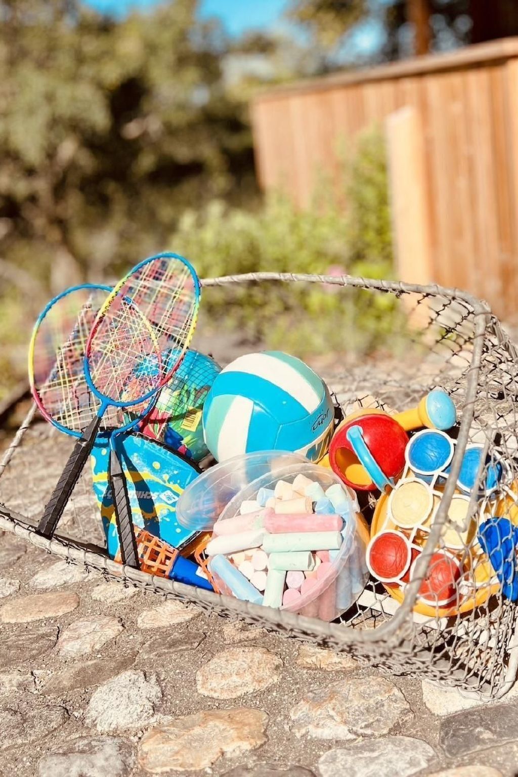 A basket filled with various sports equipment including badminton rackets, a volleyball, and colorful balls.