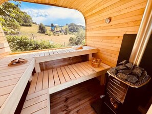 Eine Holzsauna mit einer Bank, einem Steinofen und Blick auf eine ländliche Landschaft.
