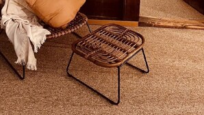 Ein gemütlicher Raum mit einem Korbstuhl, einem kleinen Tisch, einer Holztür und einem weißen Stuhl im Hintergrund.