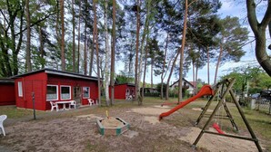 A playground with a slide and swings, surrounded by red buildings and trees. - Ferienanlage Am Sidowsee by Interhome (Fürstenberg)