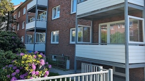 Ein mehrgeschossiges Wohnhaus mit Balkonen, Ziegel Fassade und einem Garten mit violetten Blumen.